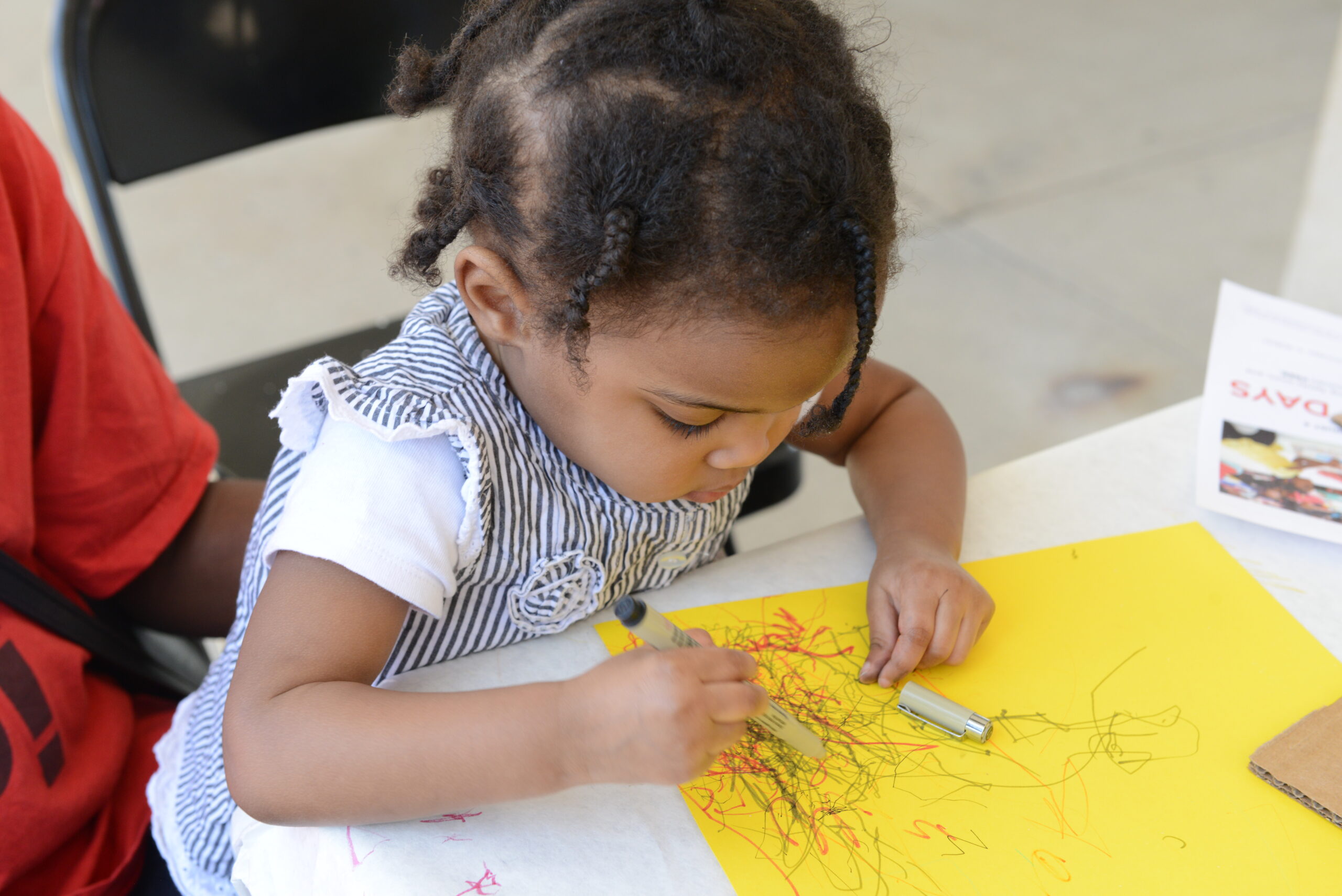 A child drawing with colored pens on yellow paper