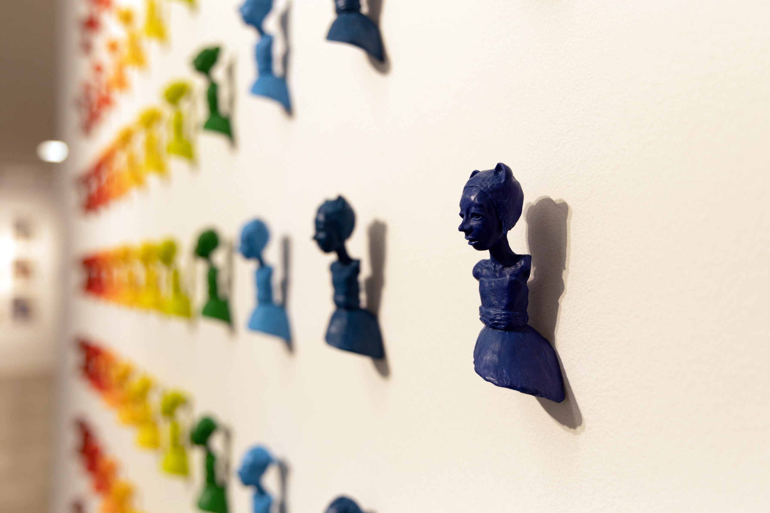 A series of small identical figures of a female form from the hips up are displayed on the wall in horizontal rows.