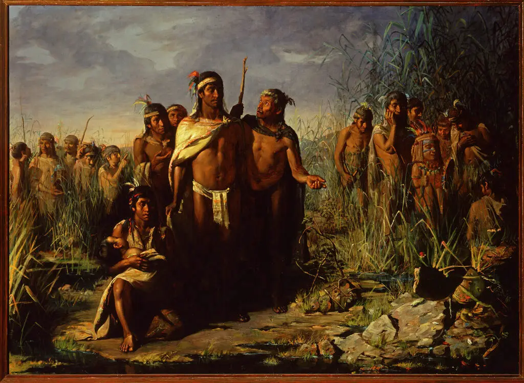 Indigenous people wearing loincloths, headbands, and feathers are assembled outdoors in an area with tall grass, corn, and rocks.