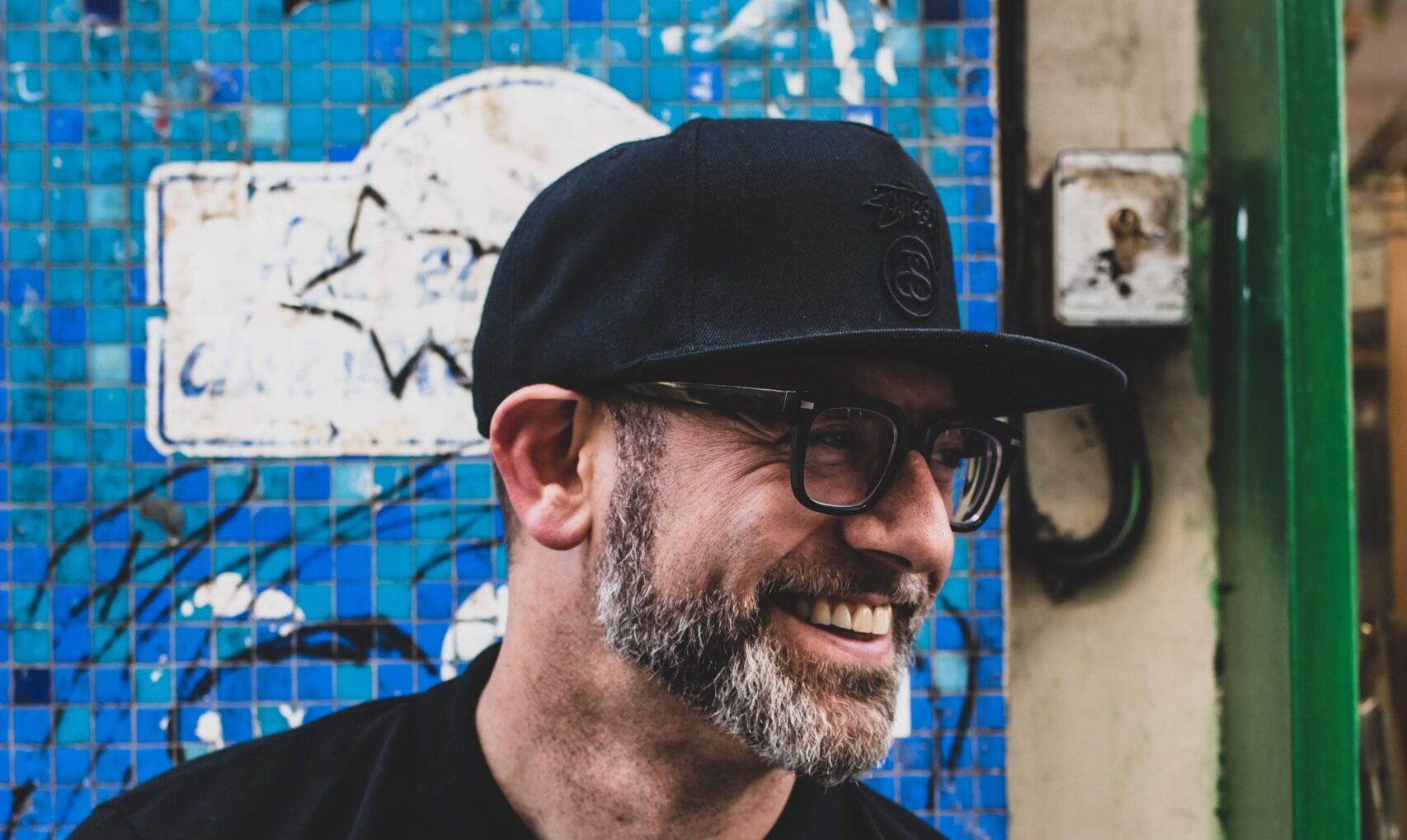 The author Kevin Coval in a black baseball cap and glasses, photographed on the street