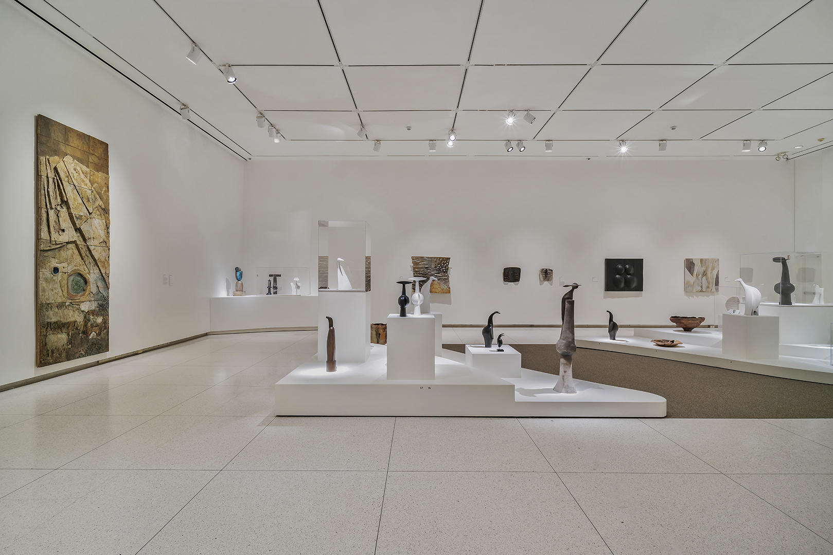A wide view of a gallery showing a plinth with ceramic sculptures of various sizes and shapes