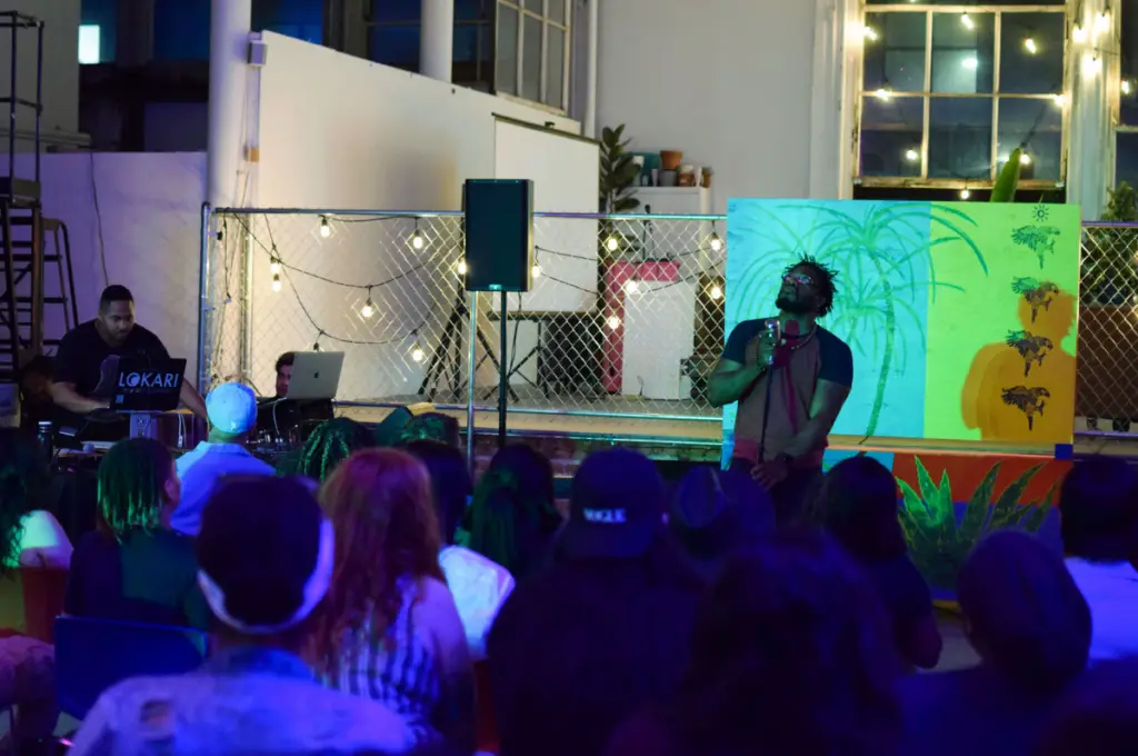 Performer stands in front of an audience seated in chairs with their backs to the camera.