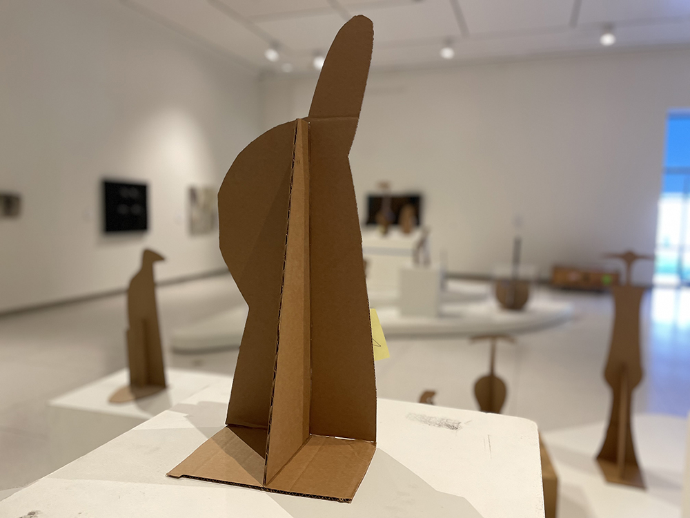 A cut-out cardboard sculpture sits on a pedestal in a museum gallery.
