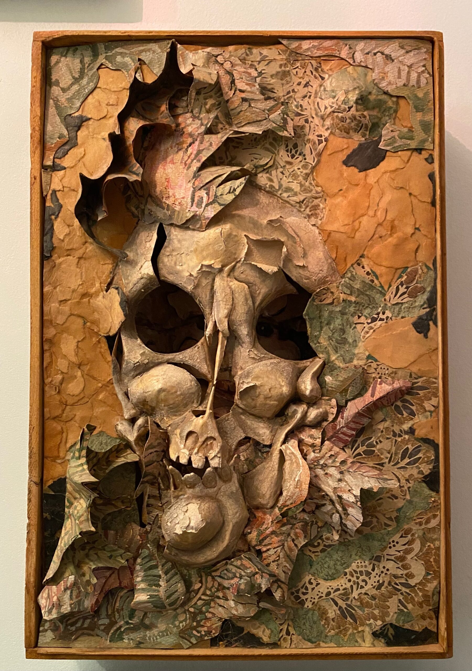 A paper sculpture of a skull surrounded by paper leaves and set inside a wooden box.