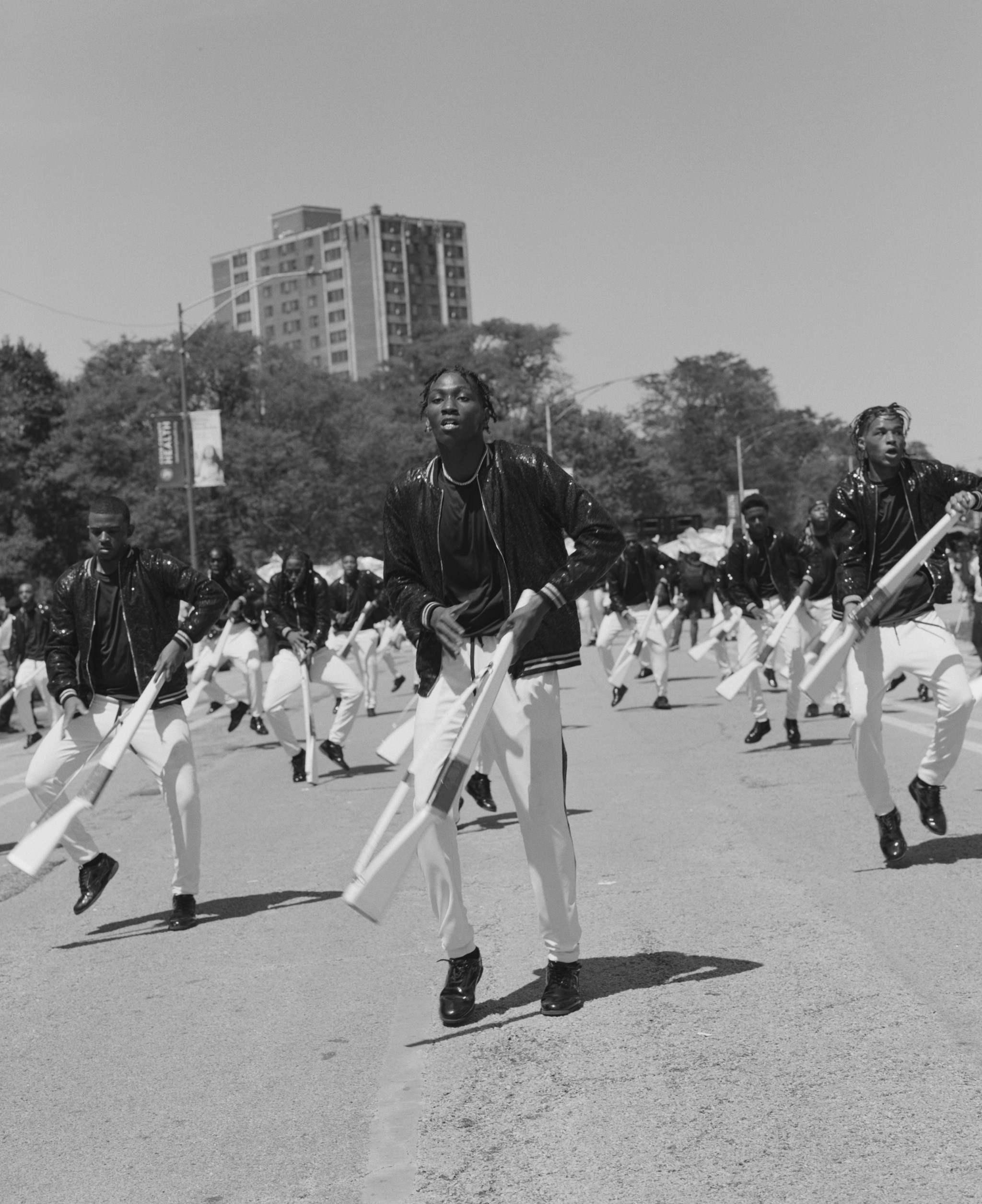Photograph of South Shore Drill Team during a performance. Performers are wearing white pants and dark jackets and twirling wooden rifles. 