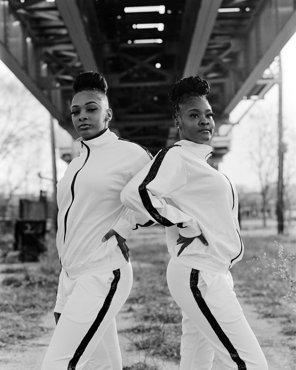Two young women from the South Shore Drill team pose in team unifrom under a bridge, facing opposite directions to one another. 
