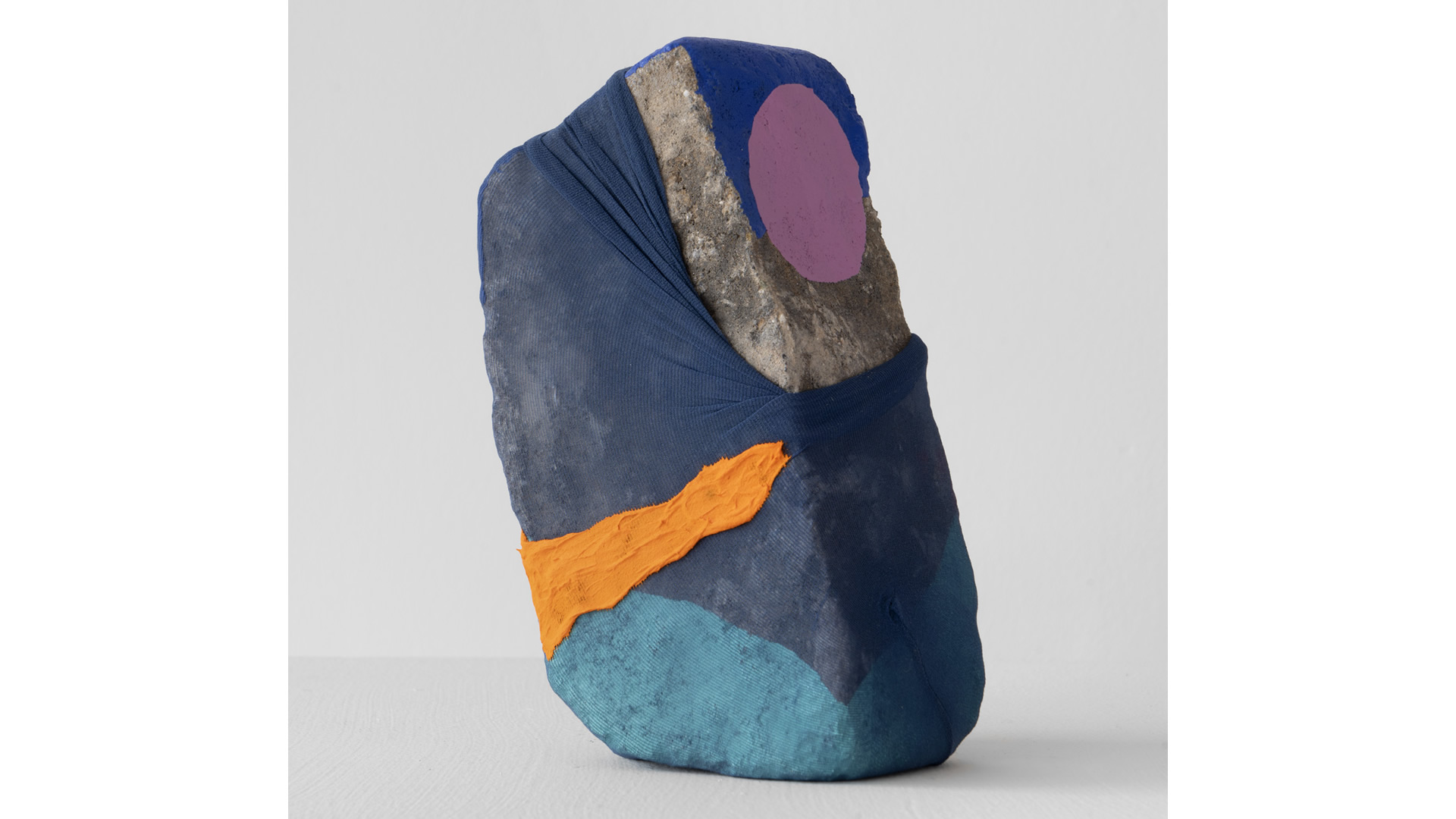 A sculpture in the form of a rock. Painted gray and covered in nylon with geometric shapes in a variety of colors.