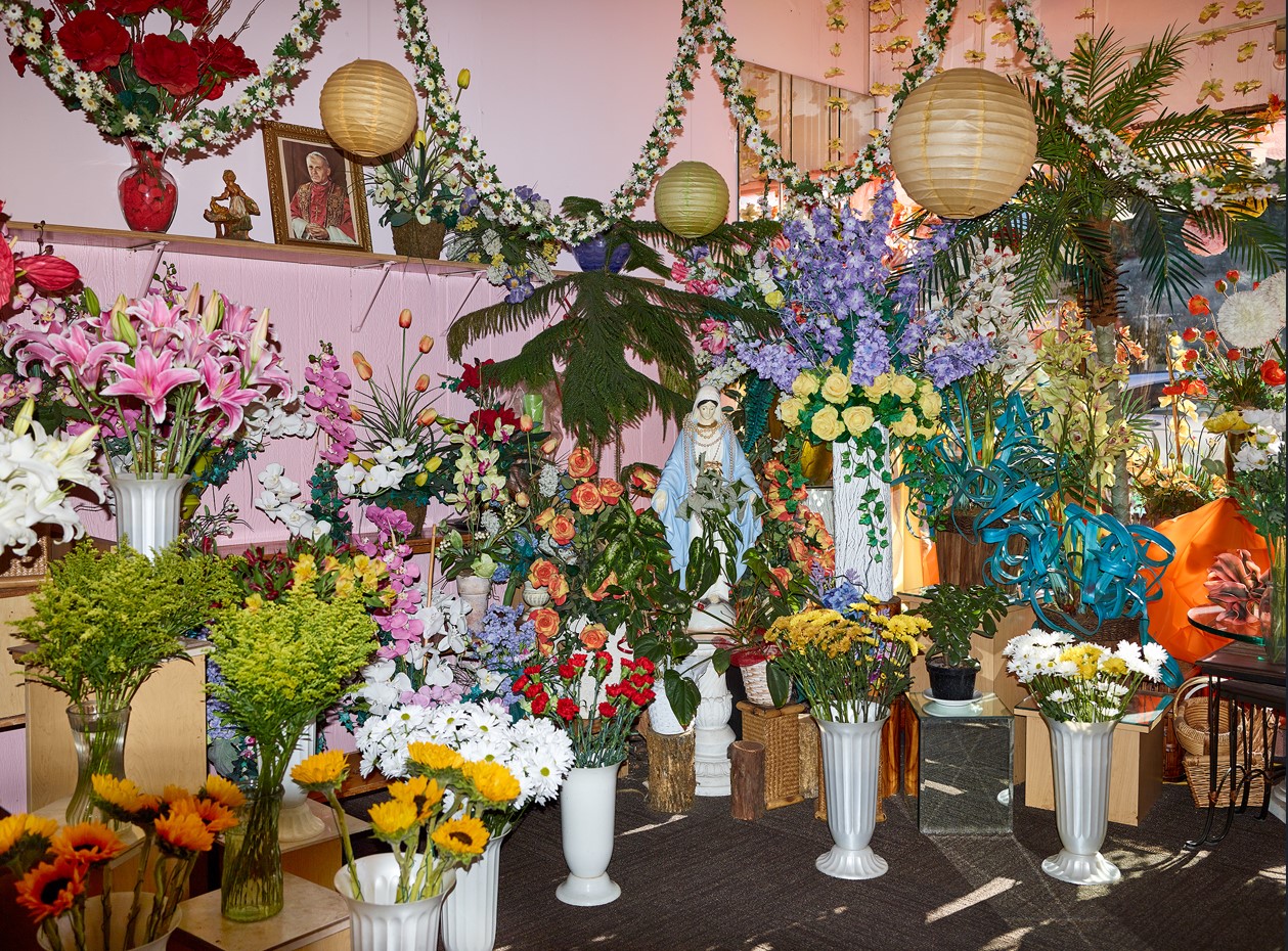 A crowded floral shop with many colorful cut flowers in white vases.