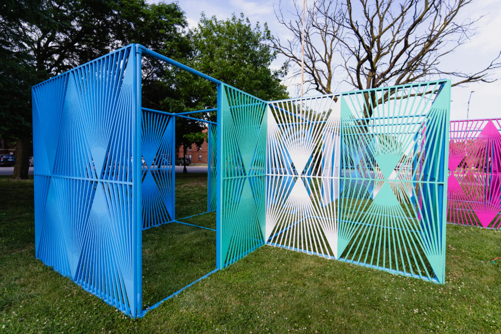 A pavilion formed from a series of colorful lattice panels installed in a park space.