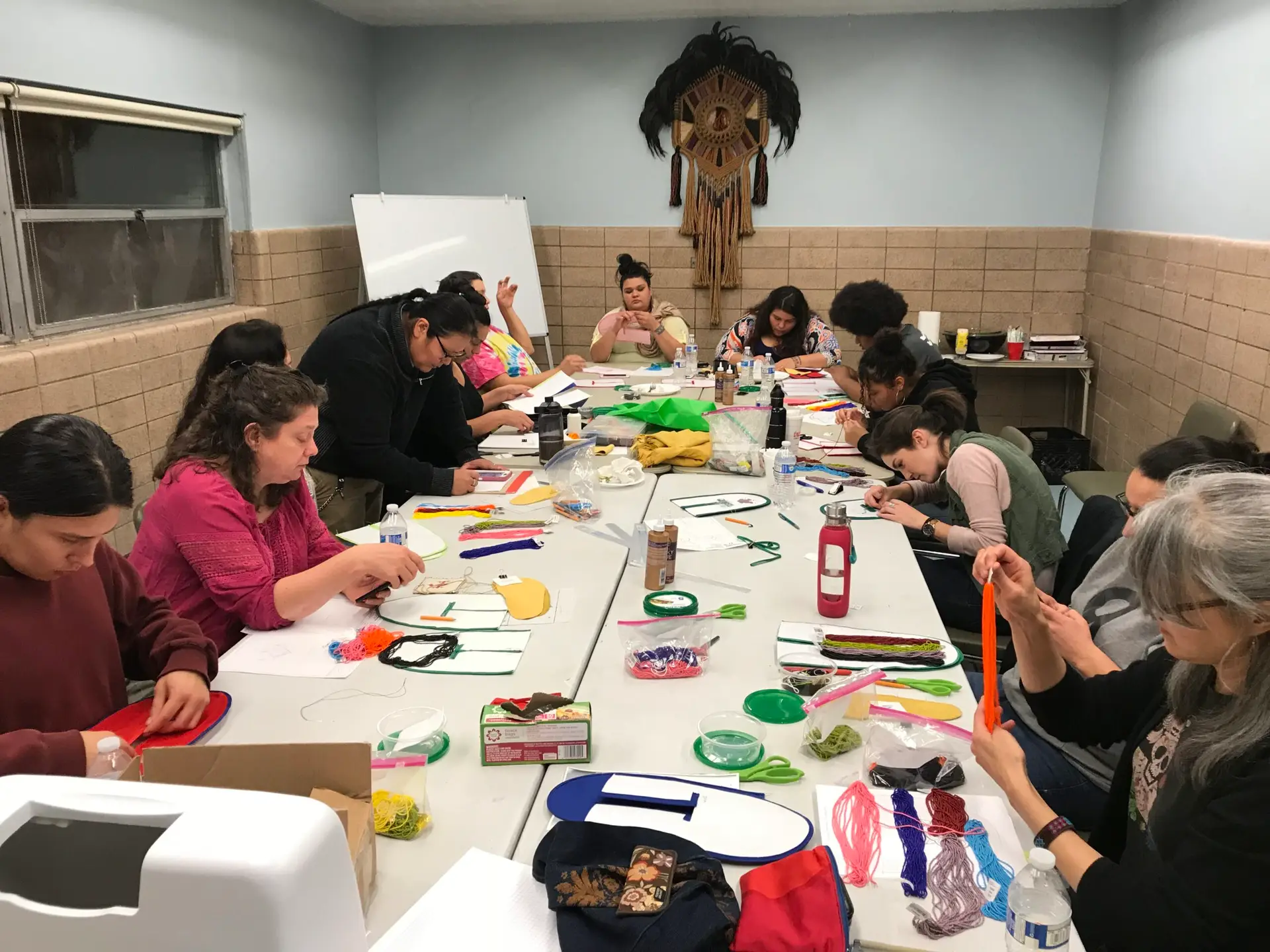 A dozen workshop participants seated around a long table covered with art materials, working on their projects.