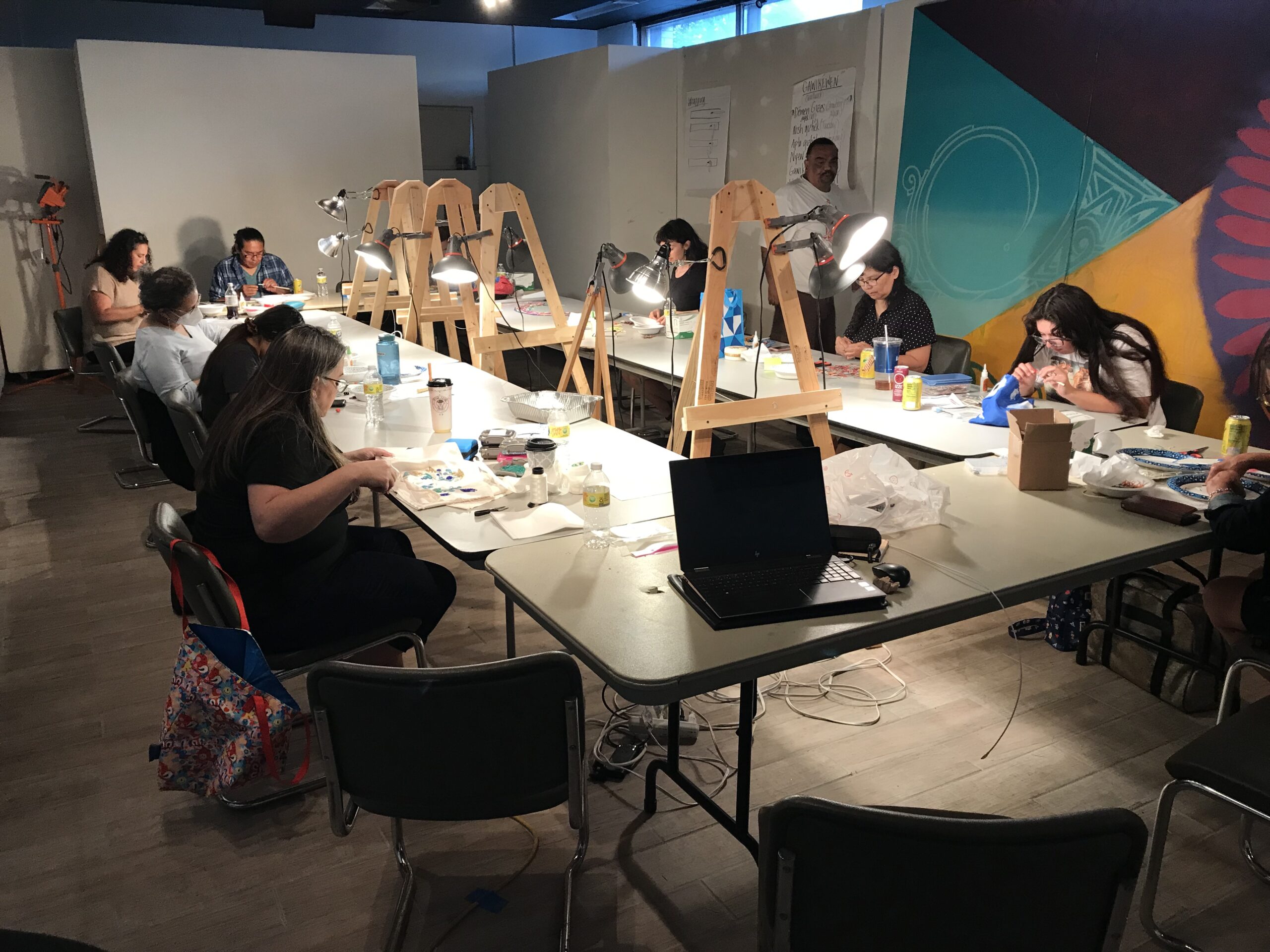 Individuals are seated at tables working on a craft project.