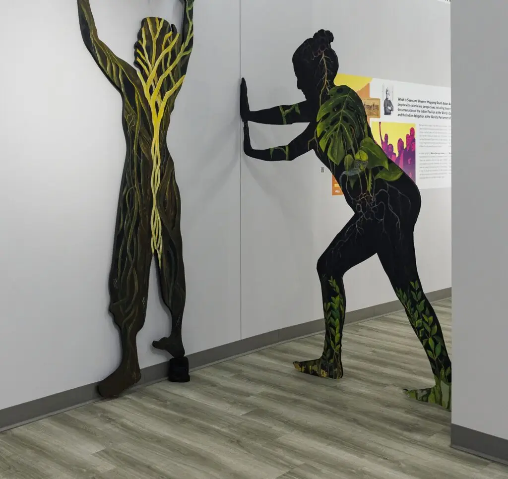 An artwork installed in a gallery space featuring two large silhouette's of human figures reaching up and forward against a wall.