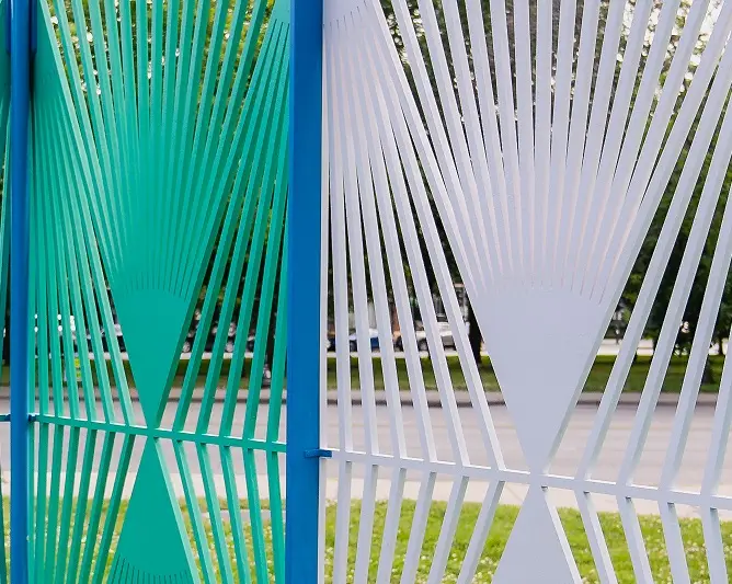 Detail of a pavilion formed from a series of colorful lattice panels installed in a park space.