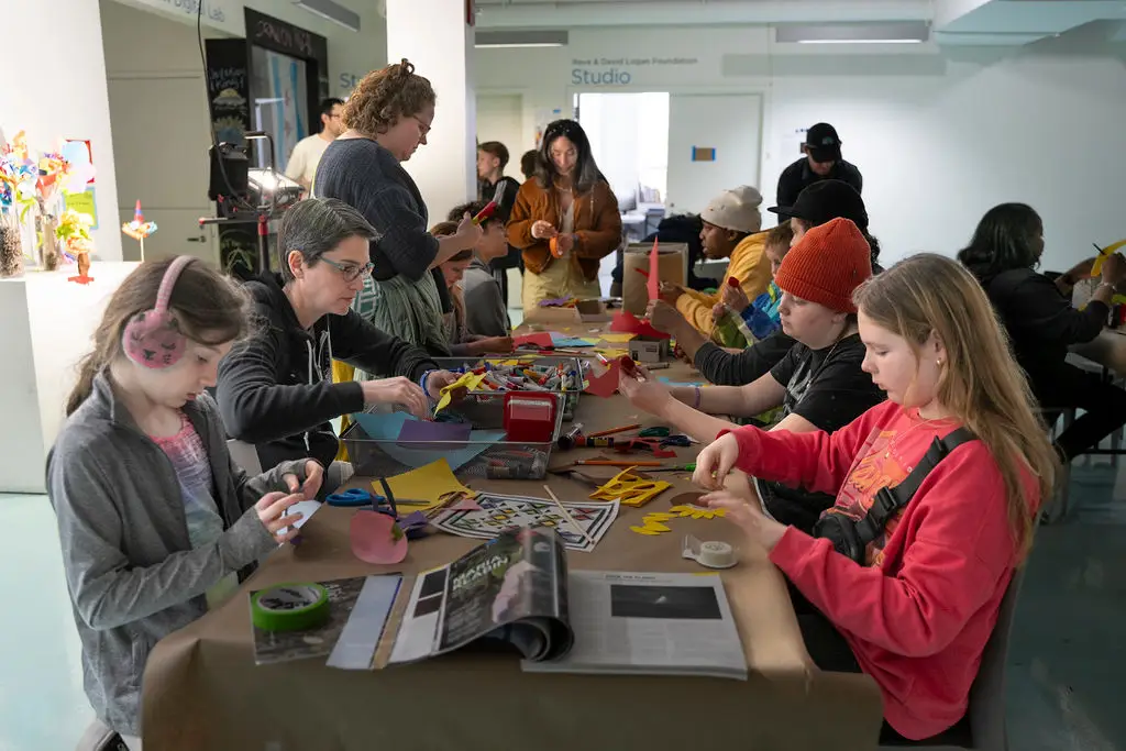 A group sits at a table covered with craft supplies working on a project.