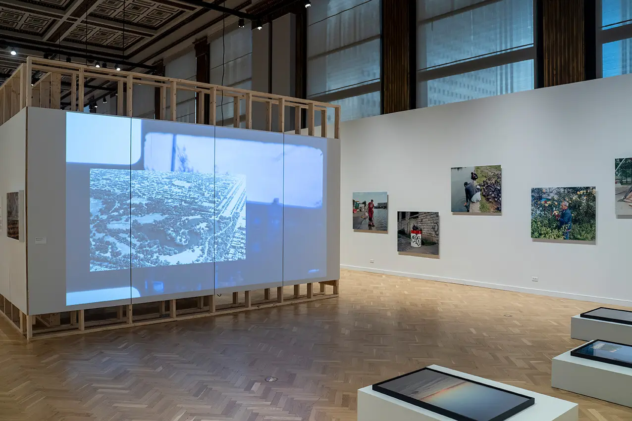 A view of a gallery space with a large video wall, 3 images on another wall, and a third image on a pedestal.