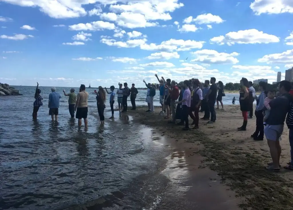 A group of people hold up their glasses in a toast on the shore of Lake Michigan.