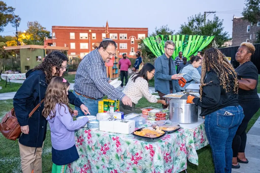 Individuals serve themselves a meal from an outdoor buffet table.