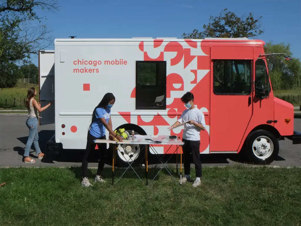 Young people work at a table in front of an orange and white truck that says "Chicago Mobile Makers."