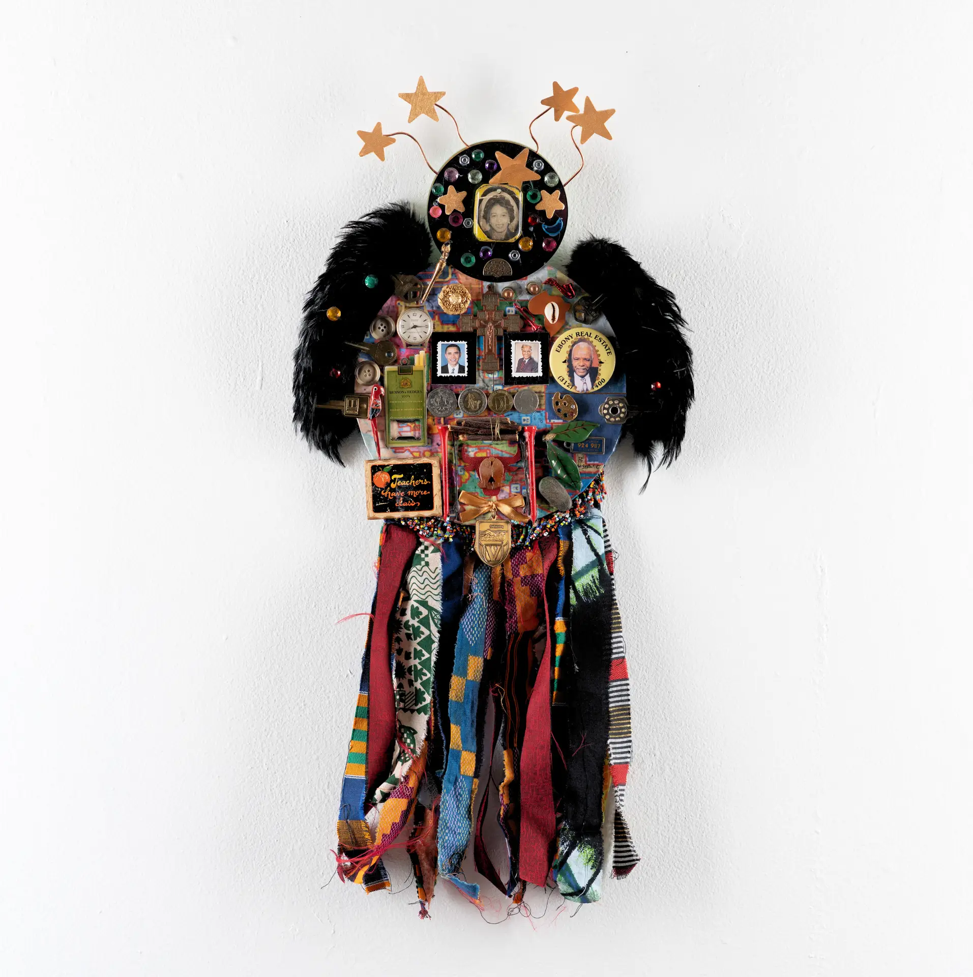 A sculpture of found materials including feathers, fabric ribbons, buttons, small portrait photos, and more.