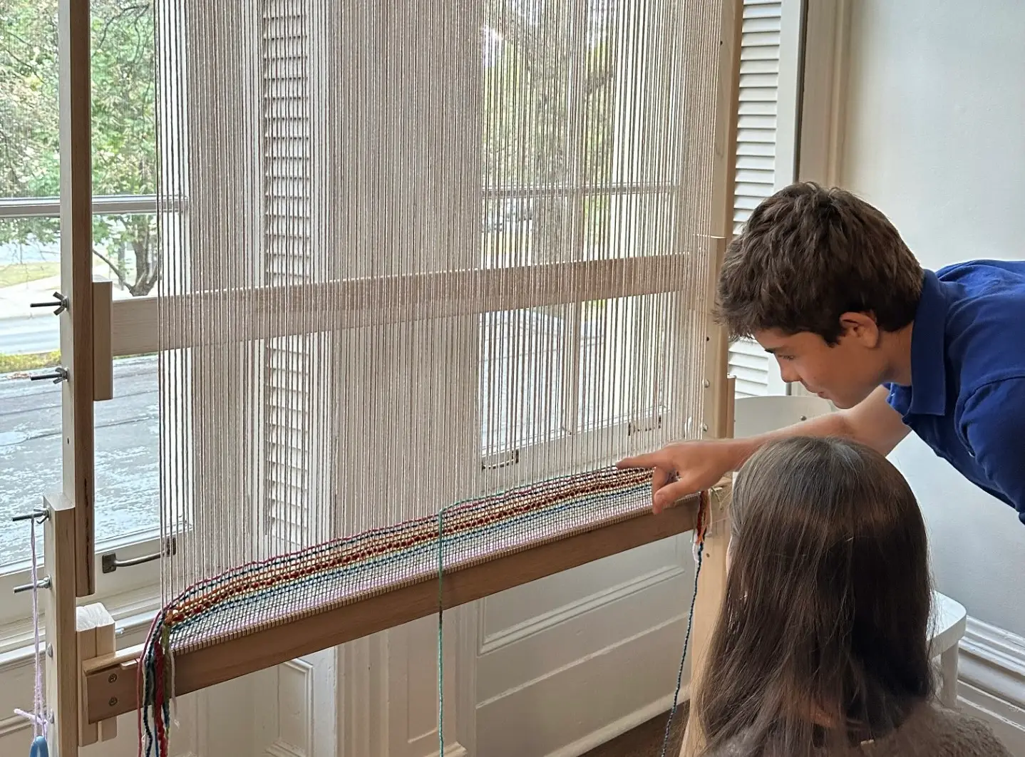 Two young visitors look at a large standing loom in front of a window of Hull-House.