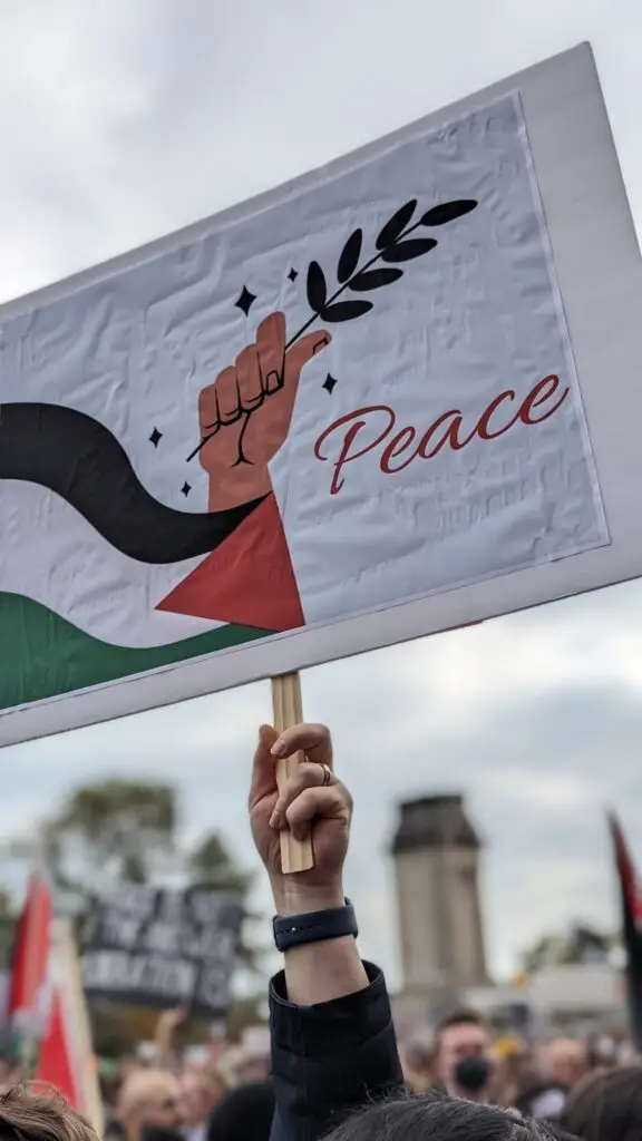 An activist holds a hand-made sign depicting bold colors and abstract figures that combine the Palestinian flag and a dove holding an olive branch.