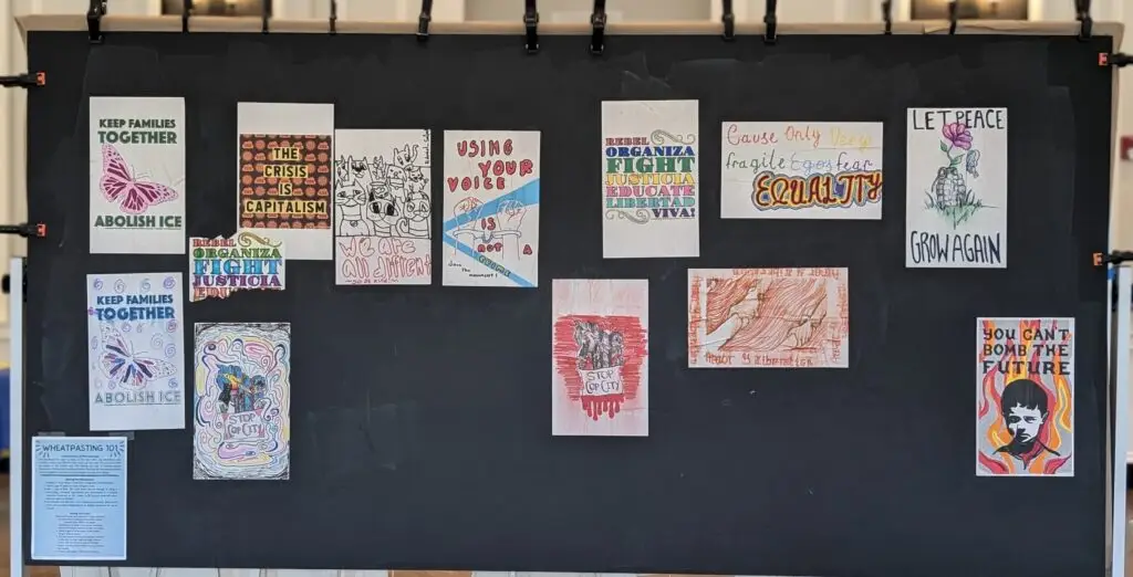 A series of small posters attached to a large chalk board wih sayins such as "Let Peace Grow Again" and "Keep Families Together, Abolish ICE."