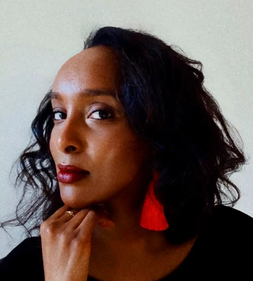 A headshot of a black woman wearing red lipstick and red triangular hanging earrings.