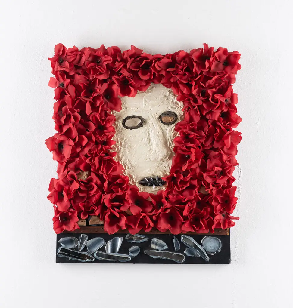 A mask surrounded by flower petals. A border of broken glass below.