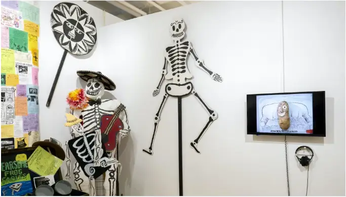 A gallery installation including large skeleton puppets and a wall-mounted video monitor.