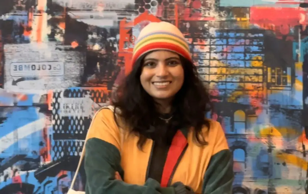 Portrait of a young woman with long black hair wearing a colorful jacket and knit hat.